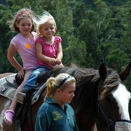 Zwei Mädchen reiten auf einem Pferd und ein Mädchen geht neben dem Pferd